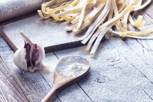 Uncooked spaghetti and rolling pin on board covered with flour