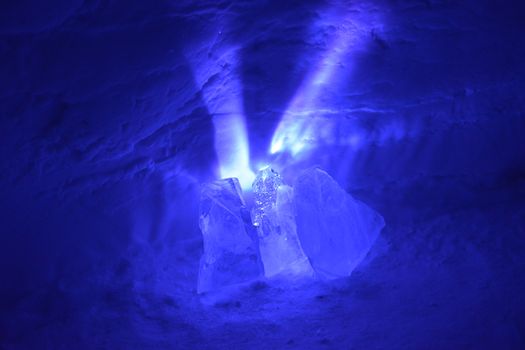 A small light source causes exploding purple rays to spread out from behind these chunks of ice. Reflections sparkle from the surrounding ice and snow. Landscape