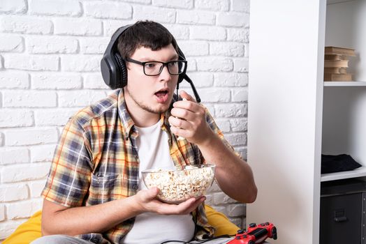 Stay home. Overeating. Unhealthy food. Young man playing video games at home eating popcorn