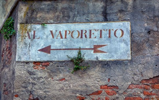 Al Vaporetto, venetian water bus. Old road sign with plants on a wall in Venice. Written in Italian