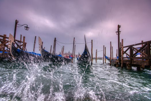 Gondolas parked at San Marco square with high tide and waves, Venice, Italy