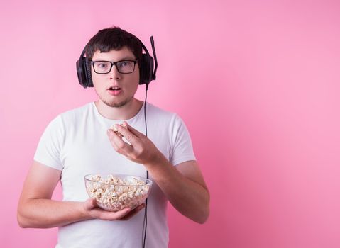 Stay home. Young mesmerized man watching a movie eating popcorn isolated on pink background with copy space