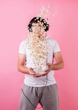 Young funny man throwing popcorn into the air isolated on pink background