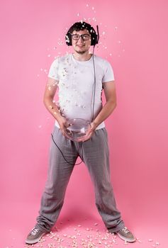 Young funny man throwing popcorn into the air isolated on pink background