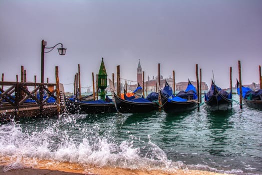 Gondolas parked at San Marco square with high tide and waves, Venice, Italy