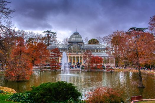 Madrid, Spain, November 30, 2019: Crystal Palace in Retiro Park in Madrid. Autumn colorful view with people, trees, plants and environment.