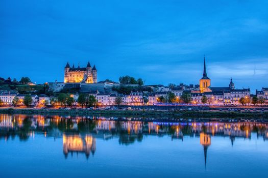 Saumur, France - April 18, 2019: Panorama of Saumur at night with the medieval castle and the old town with Saint-Pierre church, Pays de la Loire, France.