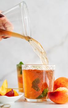 Jug with iced cold peach tea with fruit slices and mint. Iced cold peach tea poured into the glass