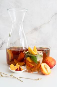 Jug with iced cold peach tea with fruit slices and mint
