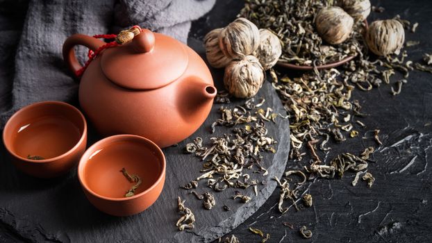 Asian teapot and scattered green tea on slate plate