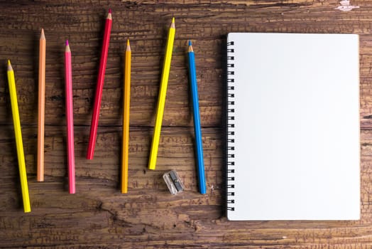 Top view of Blank notebook white paper and variegated colored pencils on brown wooden background with space for your message