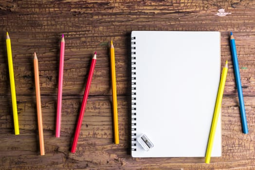 Top view of Blank notebook white paper and variegated colored pencils on brown wooden background with space for your message