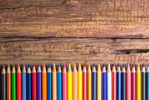 Top view of a set of colored pencils on wooden background with space for your message