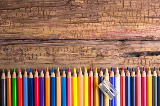 Top view of a set of colored pencils on wooden background with space for your message