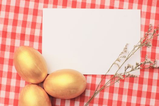 Golden easter eggs on red checkered tablecloth background with blang greeting card, happy easter holiday