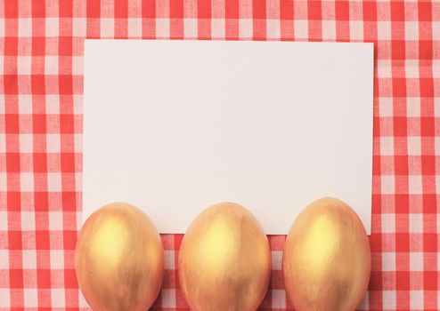 Golden easter eggs on red checkered tablecloth background with blang greeting card, happy easter holiday