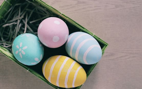 Pastel and colorful easter eggs in nest and basket on wooden background and copy space, happy easter holiday concept