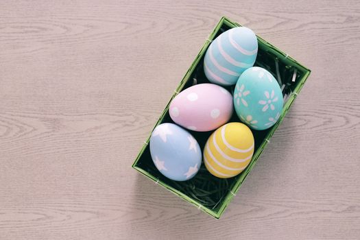 Pastel and colorful easter eggs in nest and basket on wooden background and copy space, happy easter holiday concept