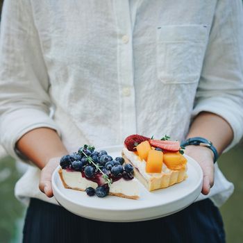 Close up woman hands holding plate of blueberry pie and mango with strawberry tart, homemade bakery style