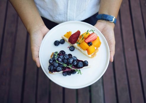 Close up woman hands holding plate of blueberry pie and mango with strawberry tart, homemade bakery style 