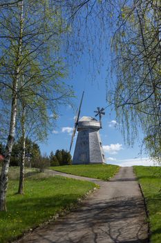 Picturesque empty country road leading to an old tower mill in rural area. Countryside landscape shot from low angle against blue sky in spring