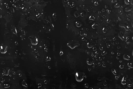 Black abstract background made drops of water on a glass