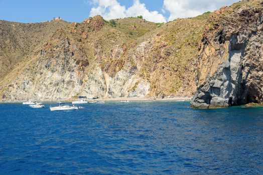 People sunbathe on small beach amongst the cliffs on Lipari Island, Aeolian Islands, Italy