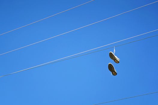 Old sneaker shoes hanging on an electric cable against blue sky