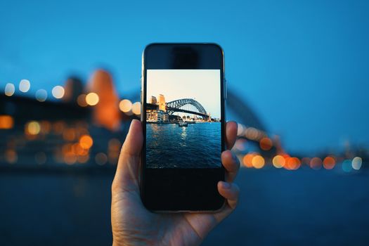 Hand holding smartphone screen taking photo of Sydney Harbour Bridge at night, Sydney in Australia