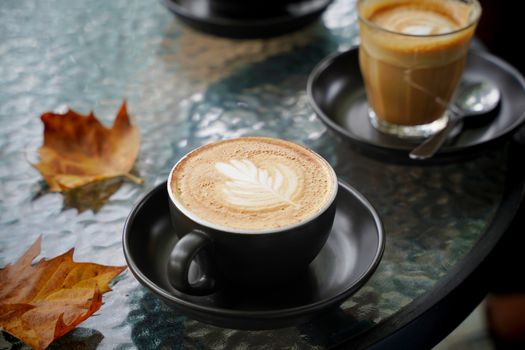 Hot cup of coffee latte and flat white with autumn leaves on the table