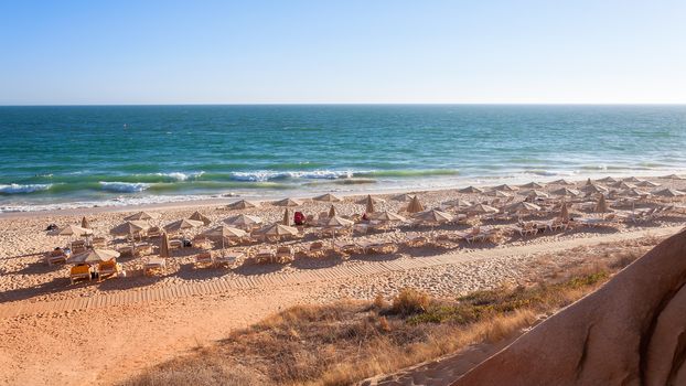 Sunbeds and umbrellas on the Falesia Beach in afternoon sun, Algarve, Portugal