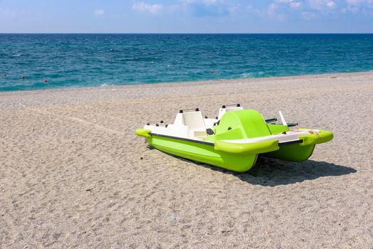 Green pedalo on a gravel beach at the Tyrrhenian Sea in Calabria, Italy