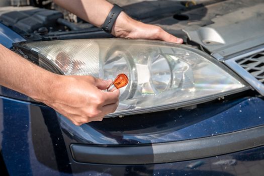 The man changes the bulb in the headlight of a car.
