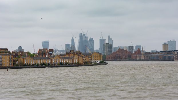 View of River Thames in London docklands with city skyscrapers in the background on a cloudy day