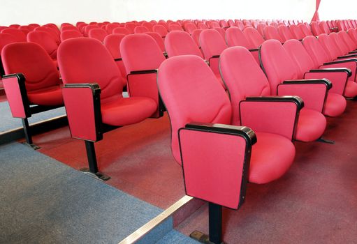 Interior view of a lecture hall wit rows of red chairs
