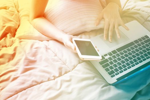 Close up Woman lying on bed with a laptop computer and smartphone on the lazy day, color transition style and gradient color 