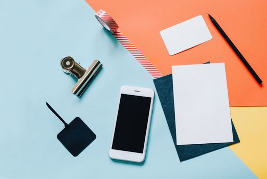 Creative flat lay style workspace desk with smartphone, blank envelope, sunglasses and masking tape on modern colorful background