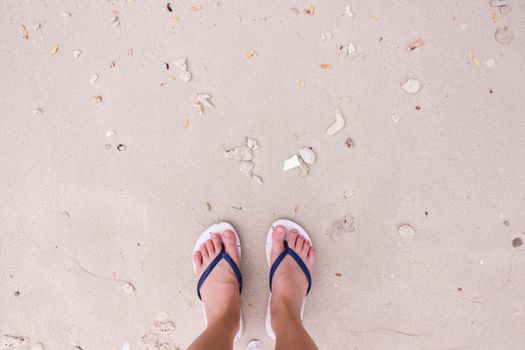 Selfie of feet in fashion sandals on sand beach background, top view with copy space