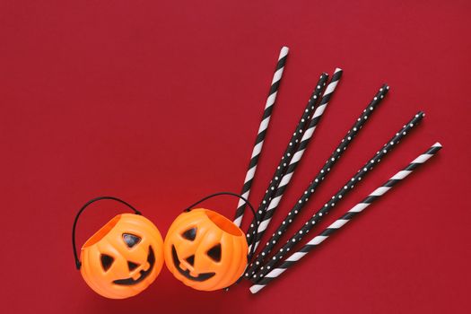 Flat lay style of halloween party concept with decorative pumpkins and black fancy straw on red background, copy space 