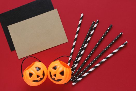 Flat lay style of halloween party concept with decorative pumpkins and black fancy straw with blank card on red background