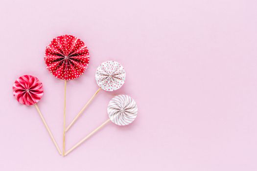 Red and white paper fan with wooden stick on pink background for party decoration