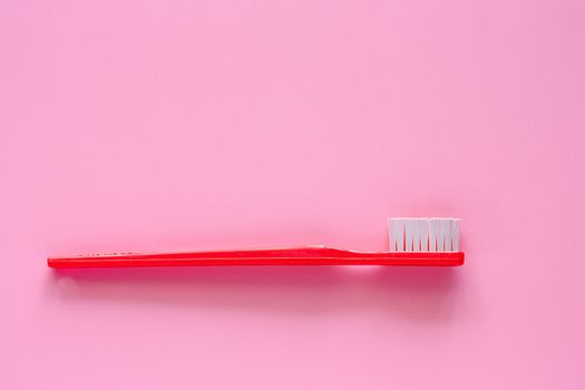 Red toothbrush used for cleaning the teeth on pink background for dental care concept