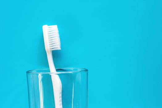 White toothbrush in the transparent glass used for cleaning the teeth on blue background for dental care concept