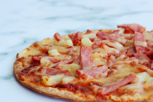 Delicious pizza with pineapple, ham slice, bacon slice, mozzarella cheese, pizza sauce on white marble background for fast food and ready to eat concept