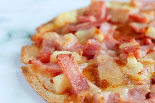 Delicious pizza with pineapple, ham slice, bacon slice, mozzarella cheese, pizza sauce on white marble background for fast food and ready to eat concept