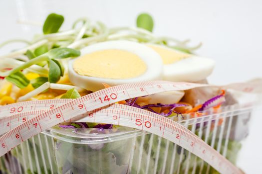 Close up of measuring tape with chicken egg and fresh salad vegetable for healthy eating and diet food concept
