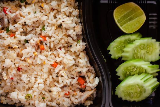 Close up of delicious fried rice with cucumber and lemon on side in lunch box for ready to eat and food concept