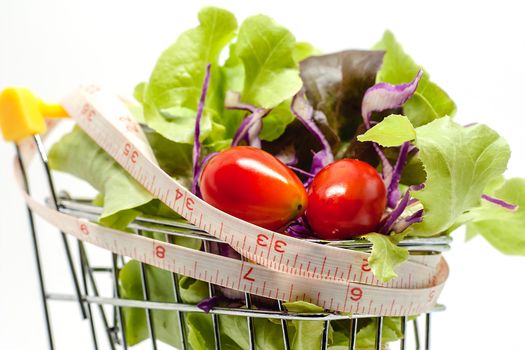 Vegetables in the shopping cart with measuring tape on white background for healthy food concept