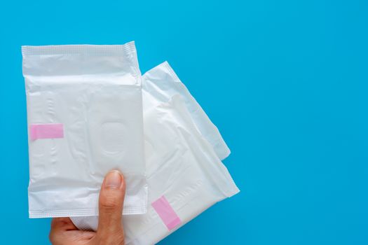Hand holding feminine sanitary napkin, an absorbent item worn by a woman while menstruating, on blue background for hygiene and health concept