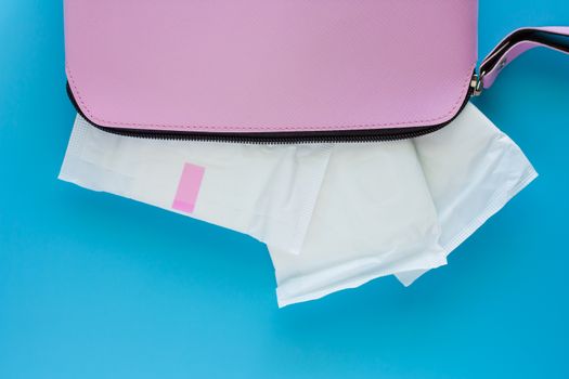 Sanitary napkin in women's pink bag on blue background for hygiene and health concept